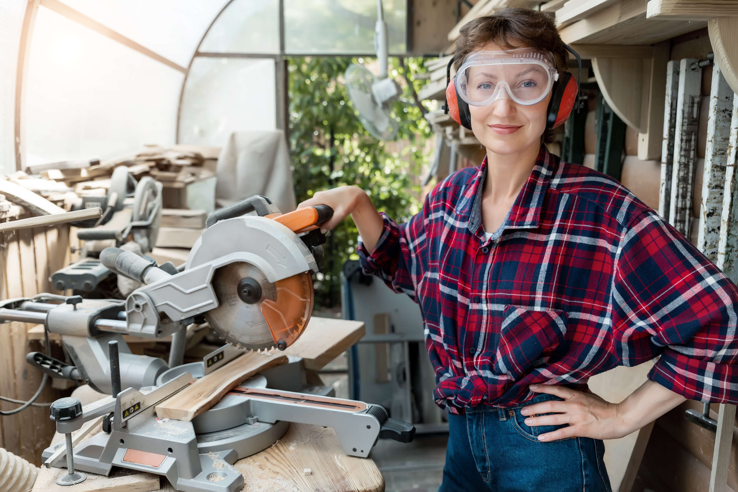 confident woman in safety goggles with saw