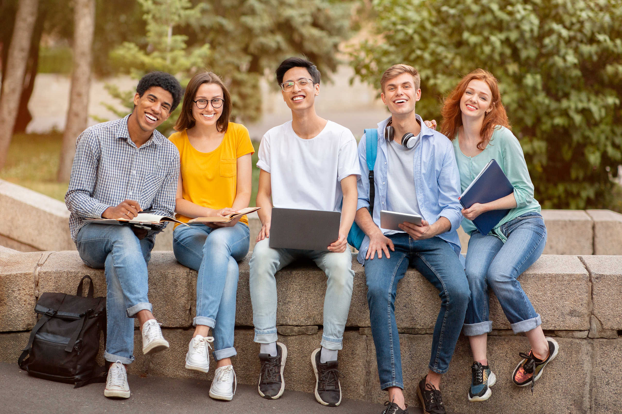 Happy Diverse Students Posing Sitting Together Outside, Smiling To Camera