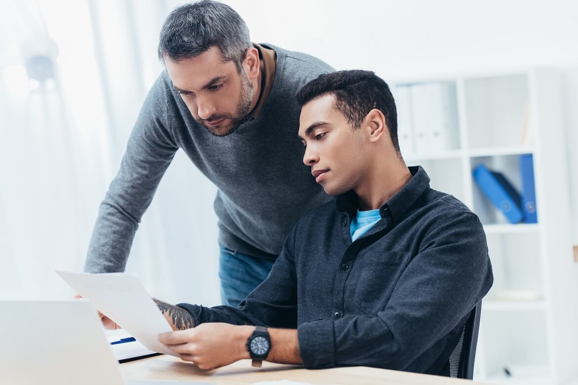 bearded mentor assisting young colleague with paperwork