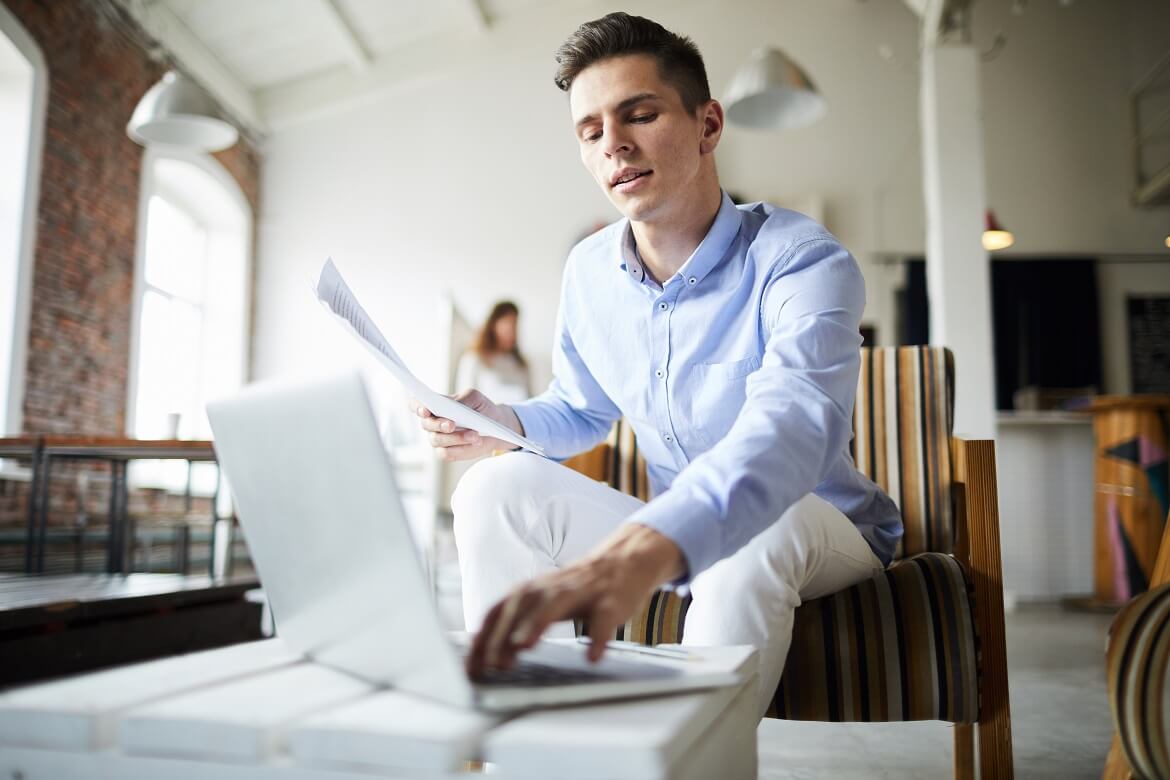 man searching on the internet with paperwork in hand