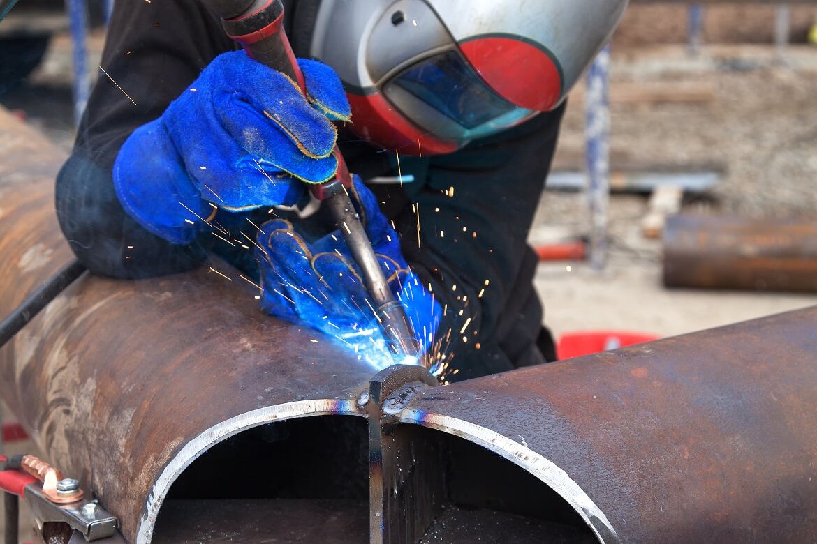 worker welding metal material in manufacturing station