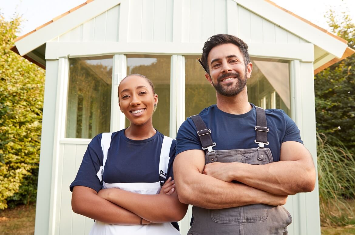 male carpenter with female apprentice standing in front of finished outdoor summerhouse