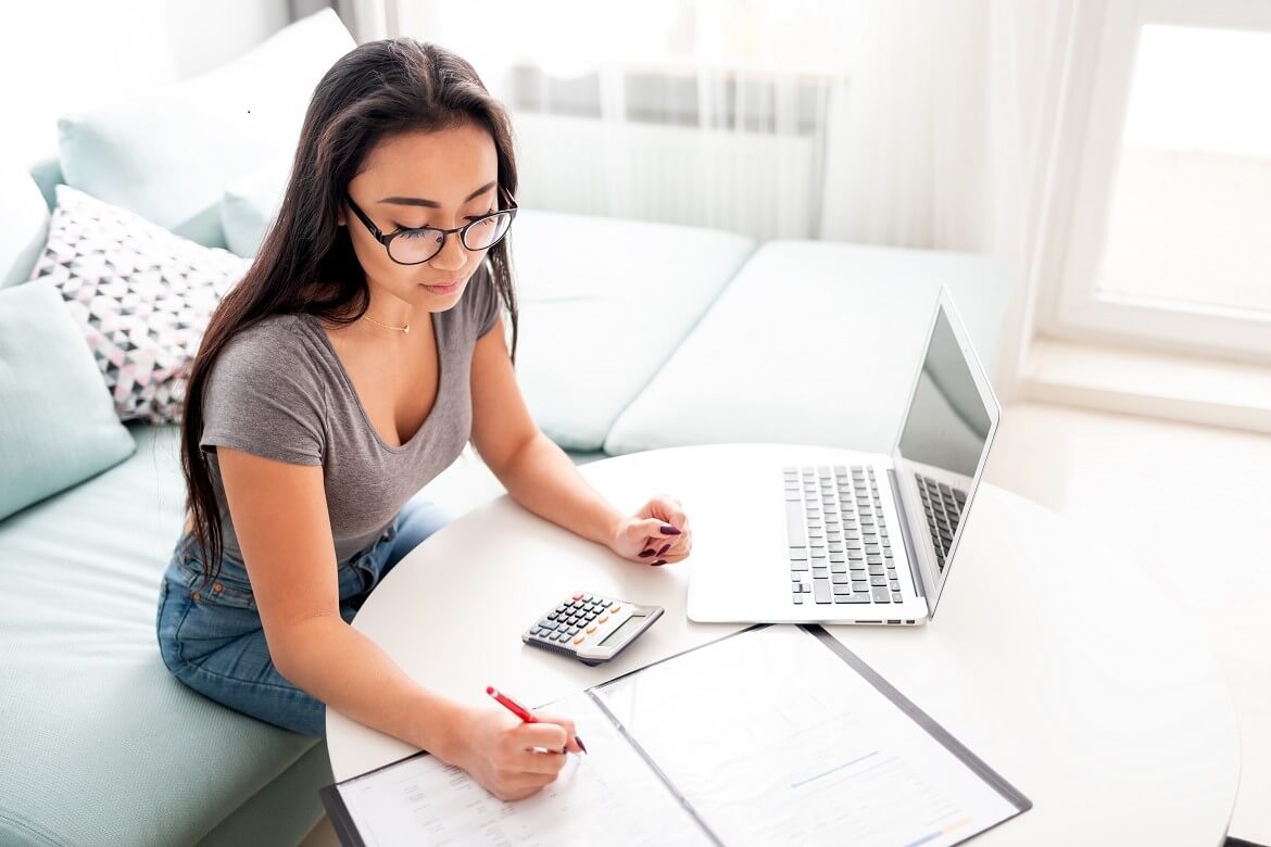 Young woman using calculator and laptop for calculations