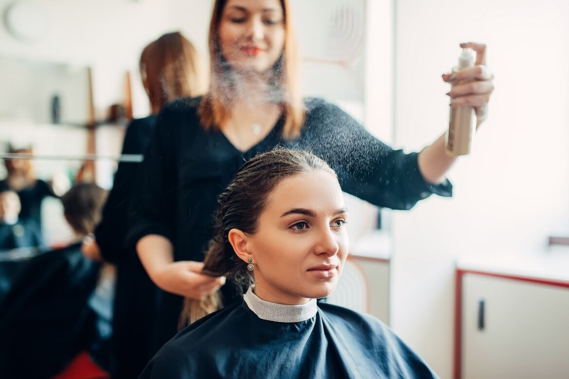 hairdresser works with hairspray while styling her client's hair