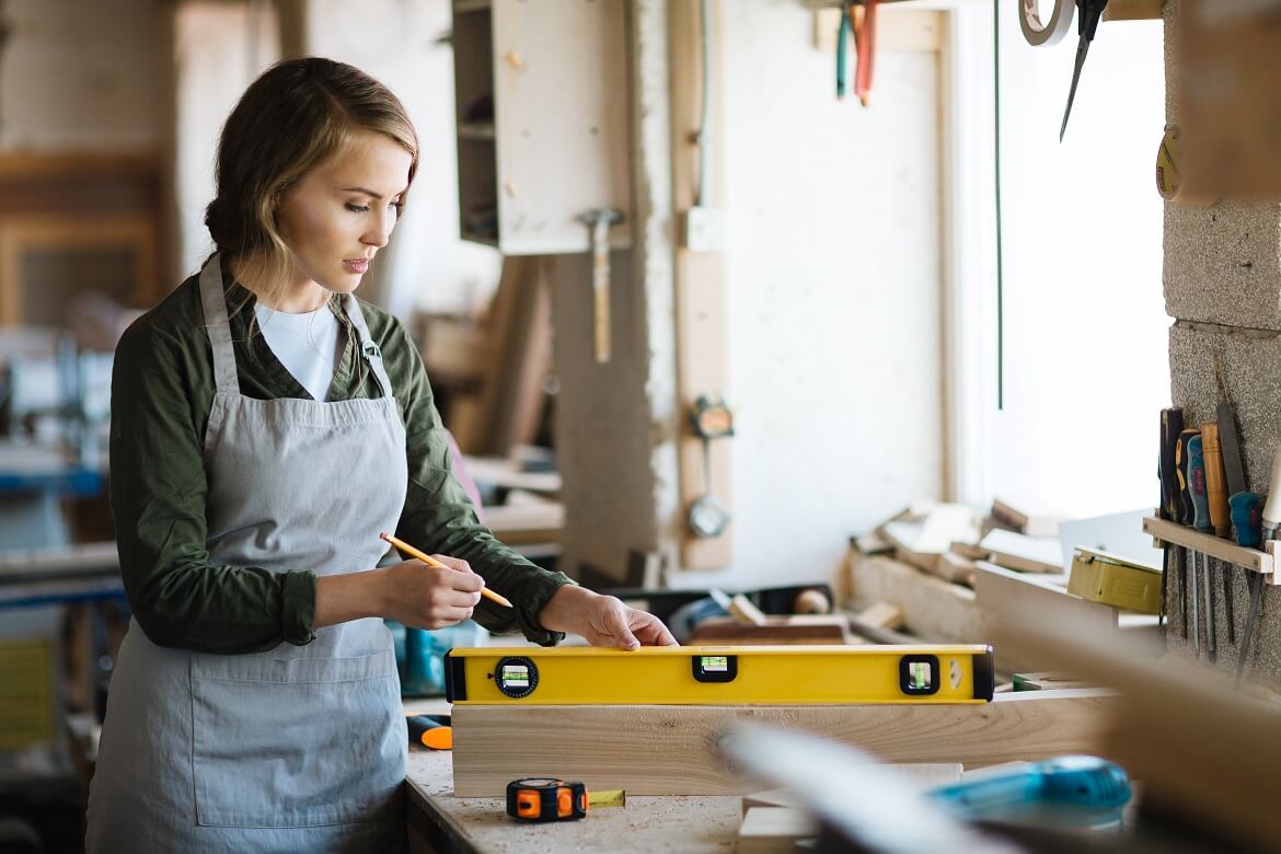 female carpenter using a leveler on a piece of wood and holding a pencil