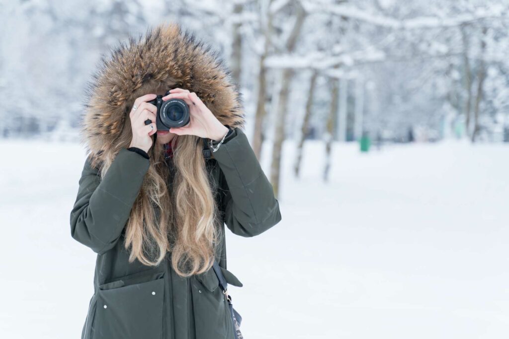 A young woman wearing a parka and taking photos with a digital camera