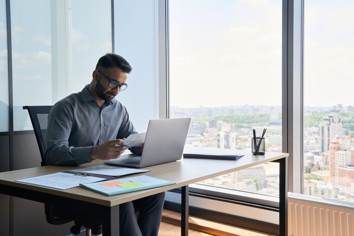Financial consultant using a laptop in his office, overlooking the city of Toronto