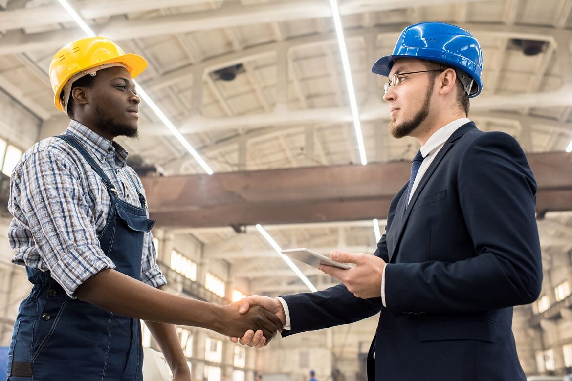 Two workers in a manufacturing facility shaking hands