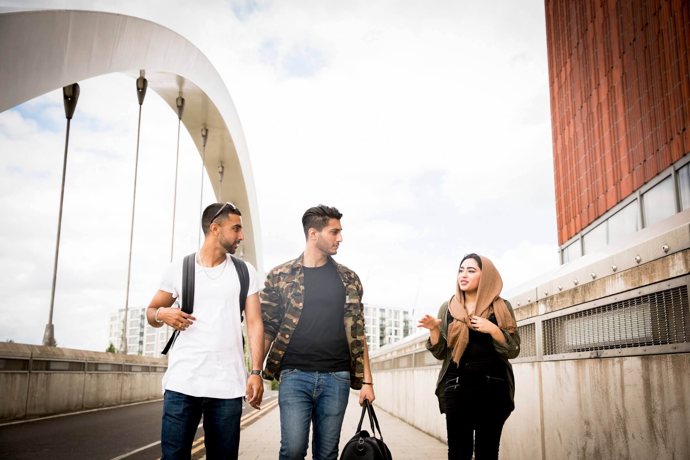 A group of young newcomers to Canada, walking and chatting while crossing a bridge