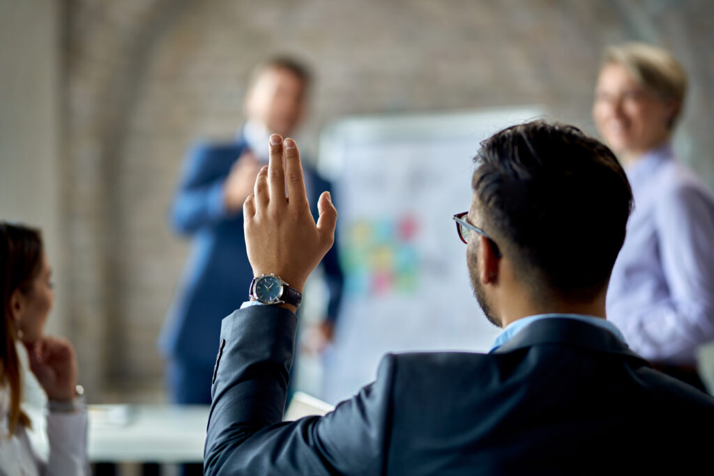 Rear view of man in blazer raising his hand in a group setting.