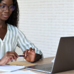 Young intelligent African black businesswoman student in glasses sitting at desk watching online learning webinar using pc laptop computer at modern home office. Distant remote work study concept.
