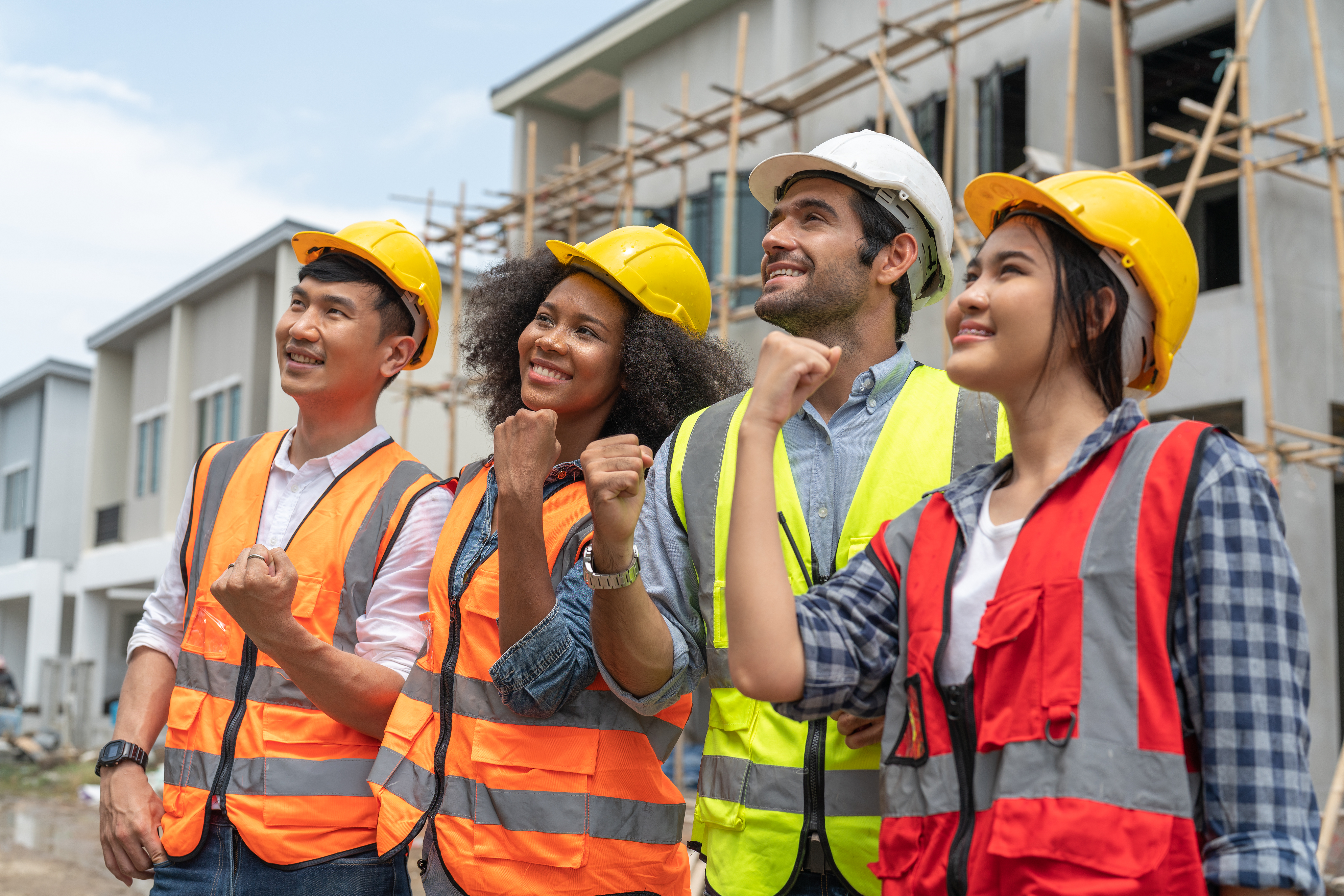 Four diverse construction workers wearing hard hats holding their fists up in solidarity.