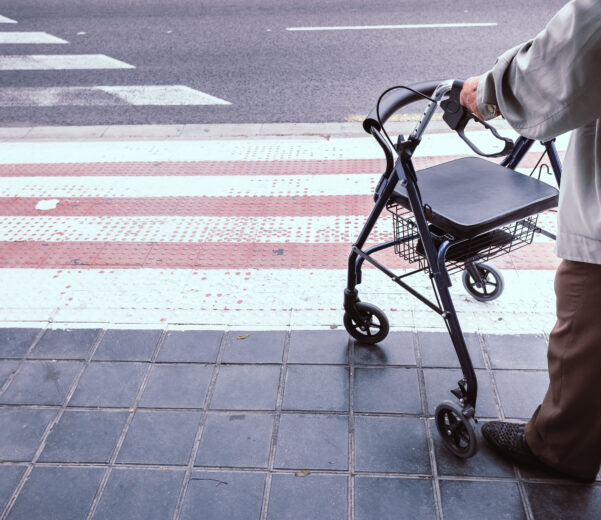 Elderly man with a disability using a walker to cross a curb cut independently outdoors.